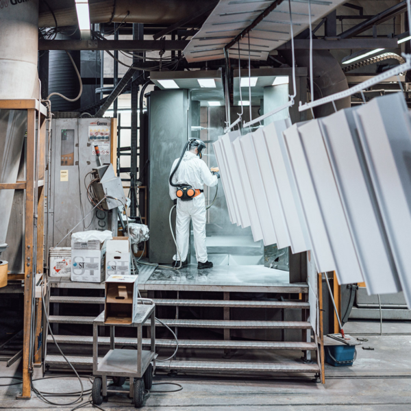 Ein Mann steht in einer Montagehalle auf einer Erhöhung und arbeitet mit Metallteilen.