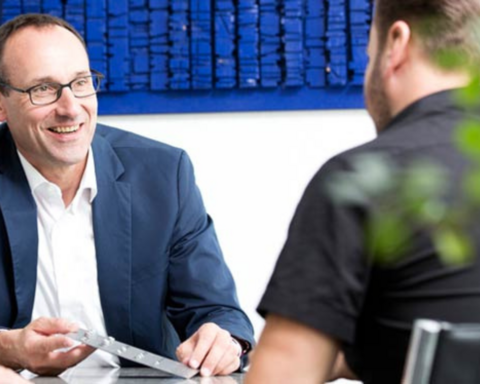 Zwei Männer sitzen sich gegenüber an einem Tisch und führen ein Beratungsgespräch.