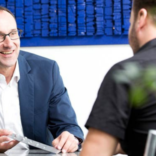 Zwei Männer sitzen sich gegenüber an einem Tisch und führen ein Beratungsgespräch.