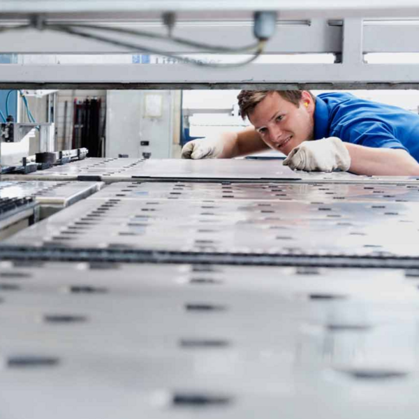 Ein Mitarbeiter in blauer Arbeitskleidung überprüft eine große Metallplatte in einer industriellen Fertigungsanlage.